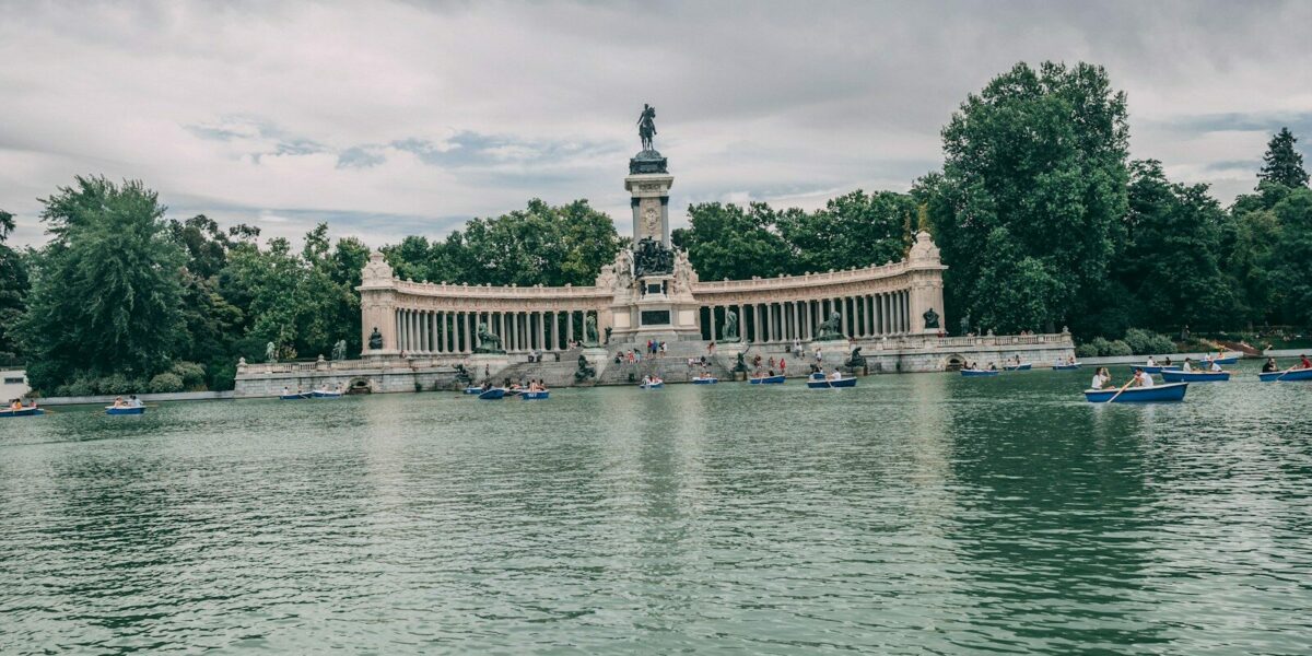 a body of water with boats and Buen Retiro Park in the background