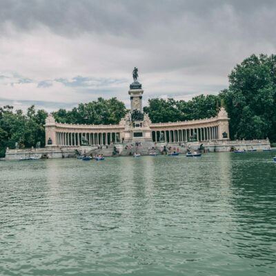 a body of water with boats and Buen Retiro Park in the background