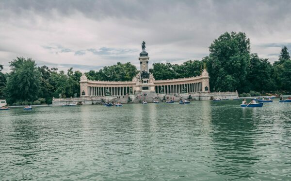 a body of water with boats and Buen Retiro Park in the background