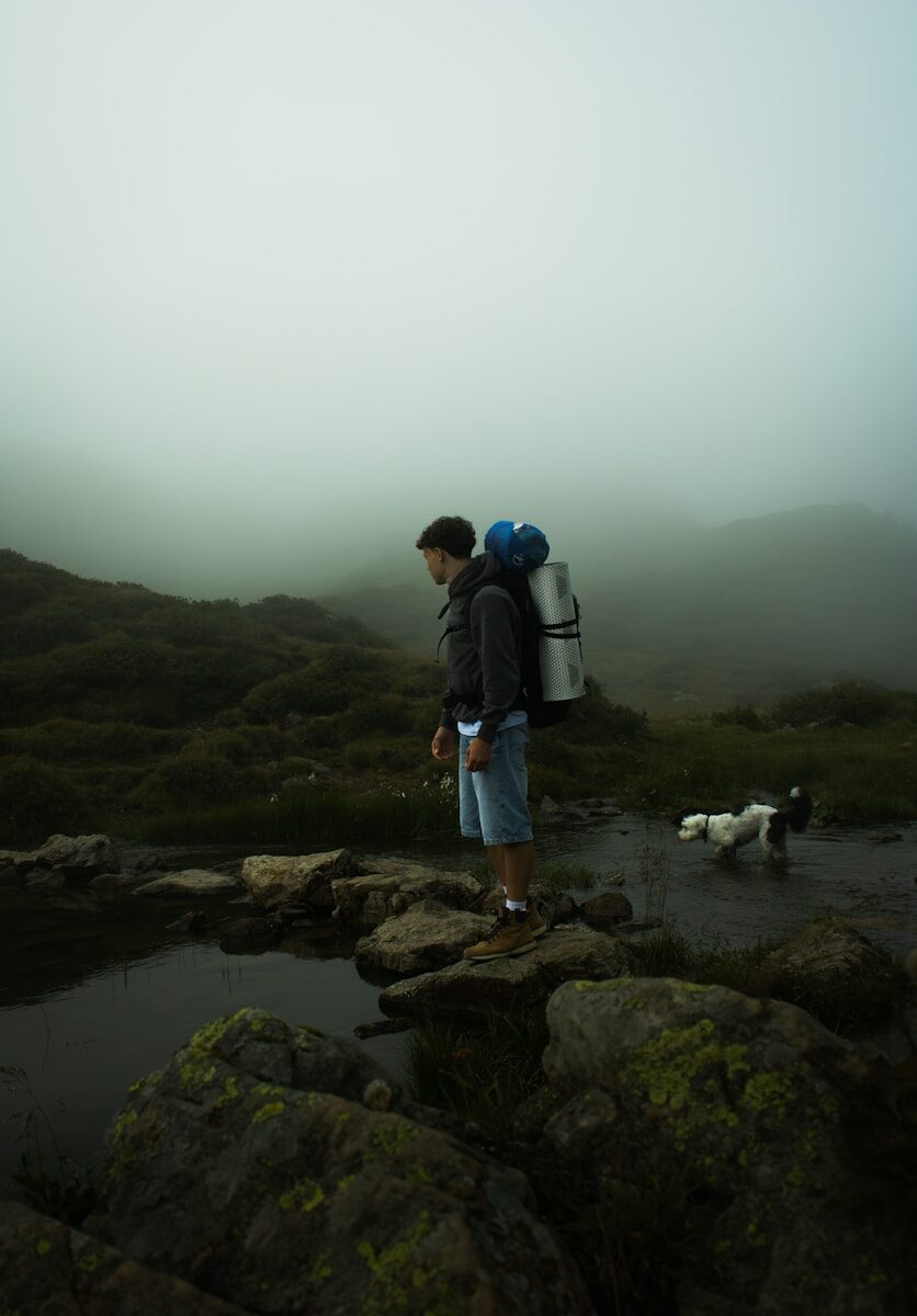 Senderista con mochila acompañado de su perro en la montaña con niebla