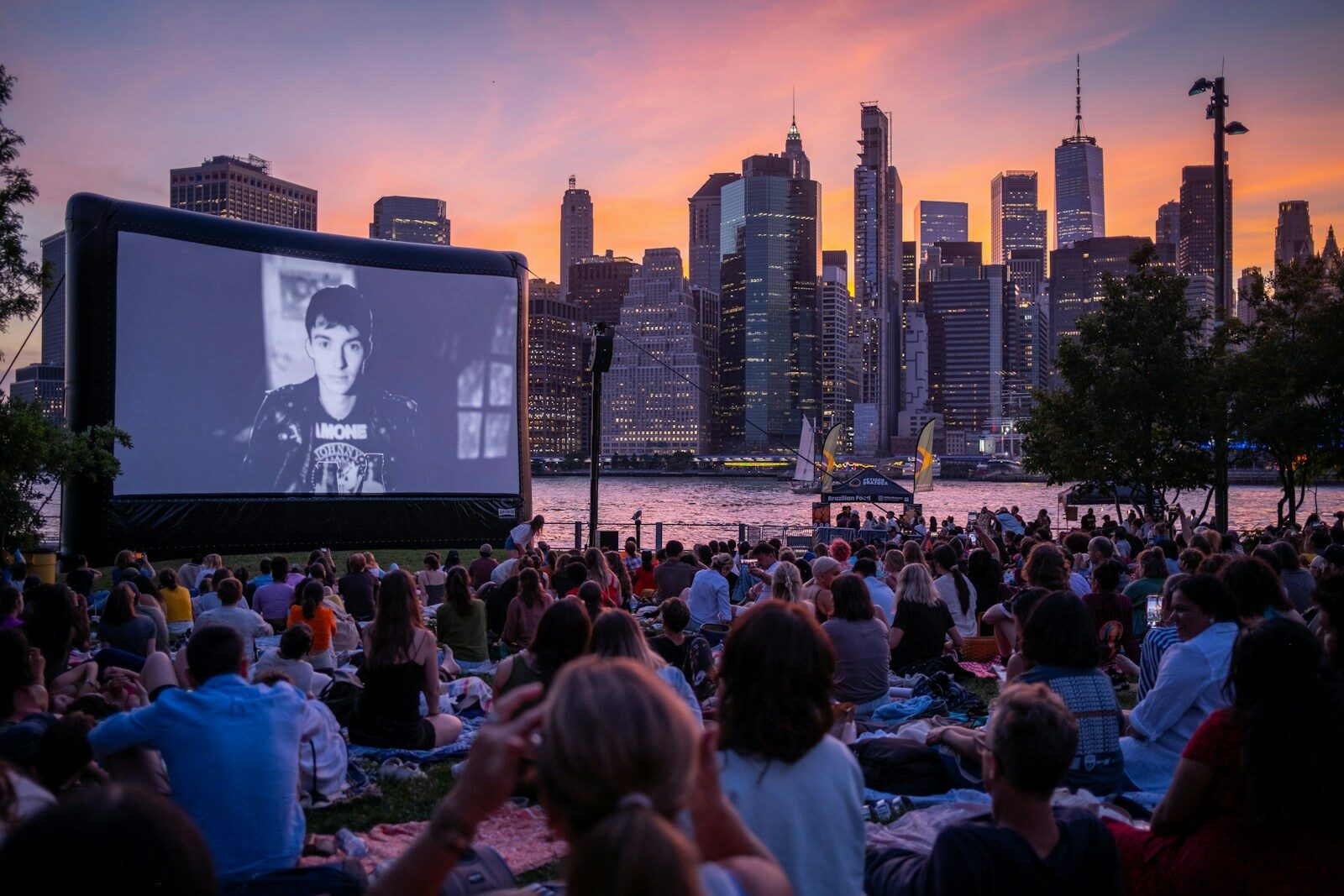 Cine al aire libre con pantalla gigante frente al skyline de la ciudad al atardecer